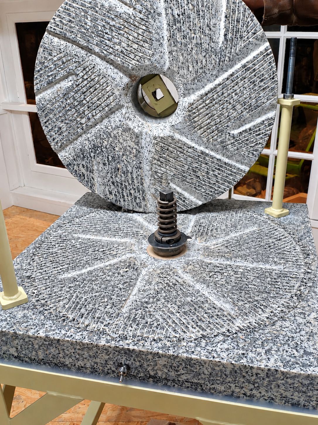 Deux meules en granit gris rainurées d’un moulin, posées sur un bâti crème dans un atelier.